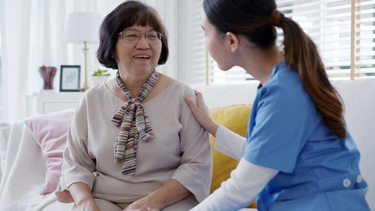 Older adult and family member reviewing a daily care checklist at a kitchen table.